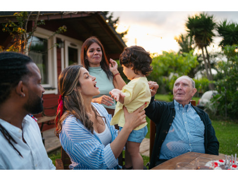 An intergenerational family at a picnic table in front of their home